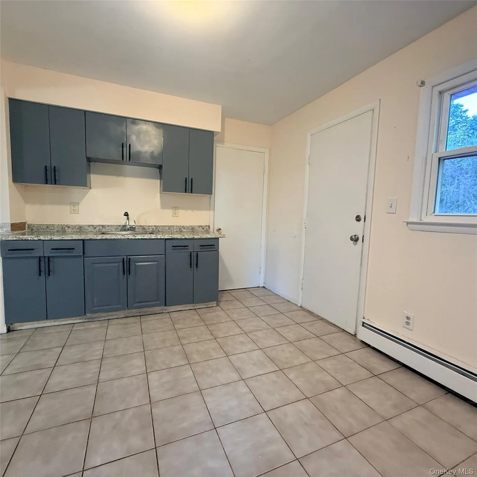 Kitchen featuring grey cabinetry, light-colored countertops, a stainless steel sink, and tile flooring Kitchen featuring grey cabinetry, light-colored countertops, a stainless steel sink, and tile flooring