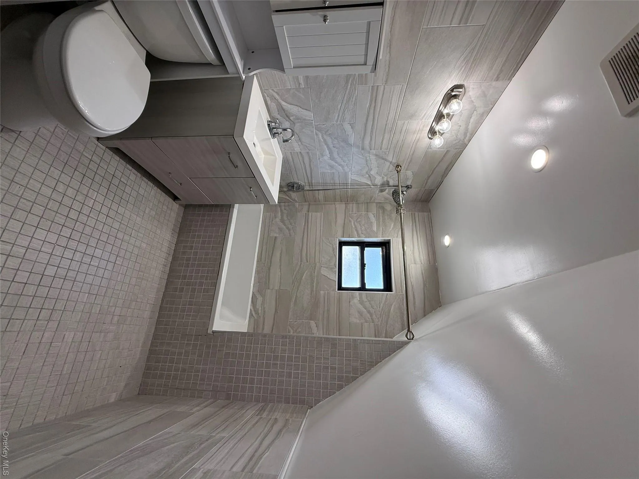 Contemporary bathroom featuring a white vanity with integrated sink, patterned floor tiles, light-toned wall tiling, and a built-in bathtub with shower Contemporary bathroom featuring a white vanity with integrated sink, patterned floor tiles, light-toned wall tiling, and a built-in bathtub with shower