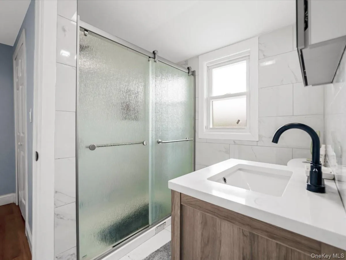 Primary Bathroom: Updated bathroom featuring a wood-finish vanity, white countertop, undermount sink, and sleek matte black faucet. Primary Bathroom: Updated bathroom featuring a wood-finish vanity, white countertop, undermount sink, and sleek matte black faucet.