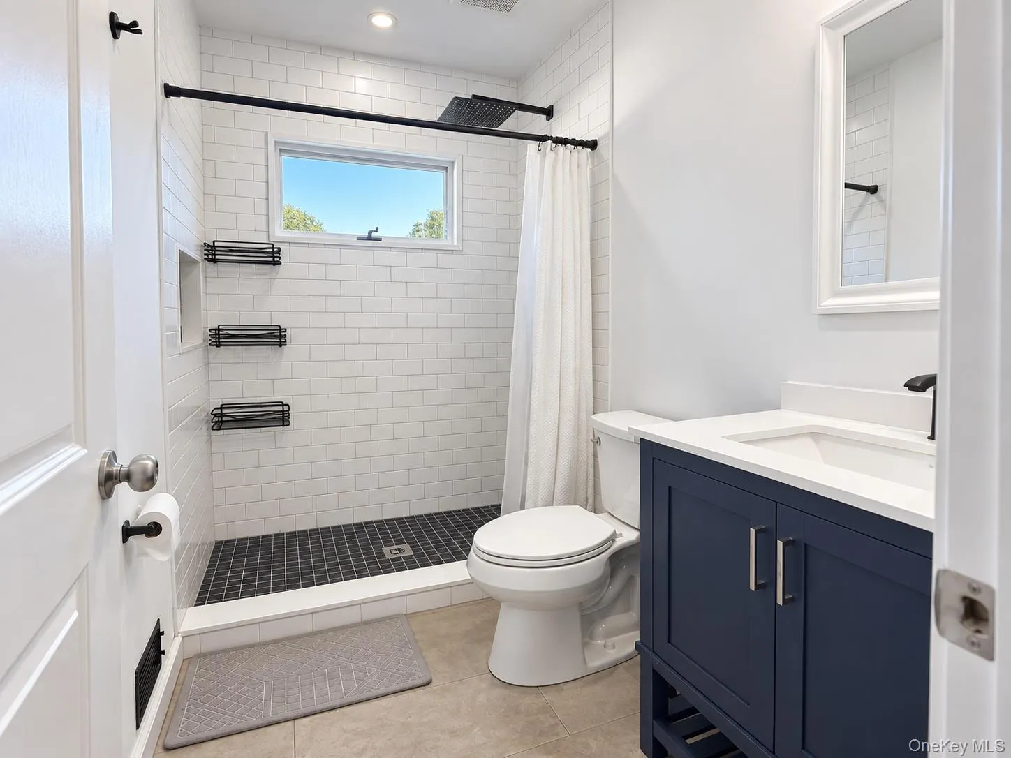 Bathroom featuring a tiled walk-in shower with built-in shelving, a window, a single vanity with a white countertop, and a dark blue vanity cabinet Bathroom featuring a tiled walk-in shower with built-in shelving, a window, a single vanity with a white countertop, and a dark blue vanity cabinet