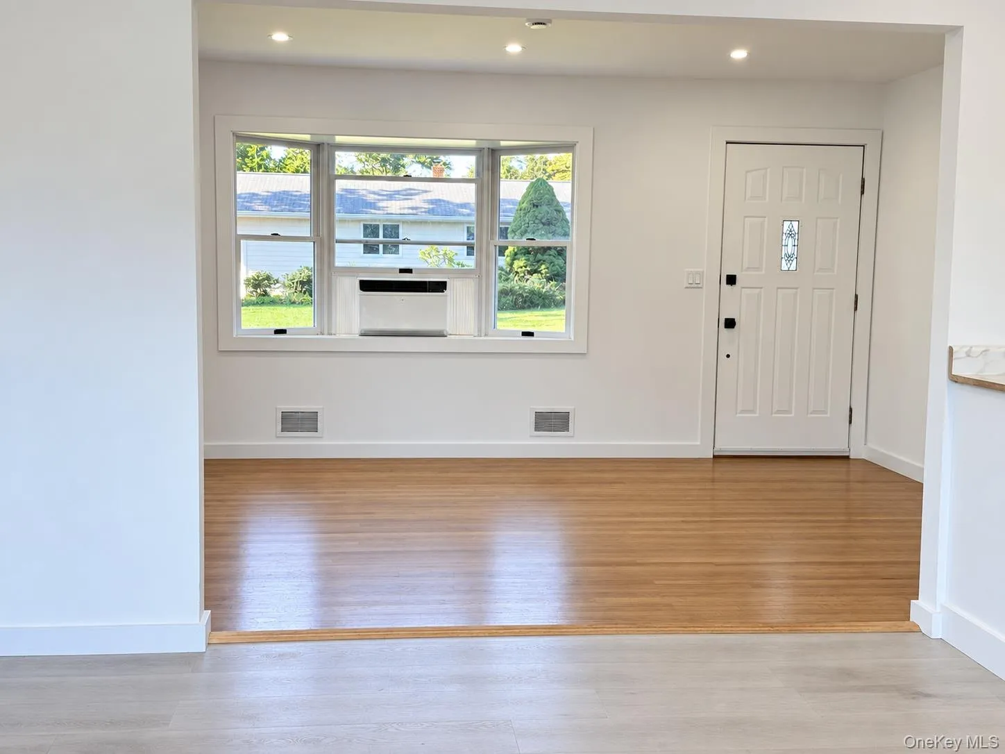 Recessed lighting, wood-finish flooring, white paneled entry door with decorative glass insert, and a bay window Recessed lighting, wood-finish flooring, white paneled entry door with decorative glass insert, and a bay window