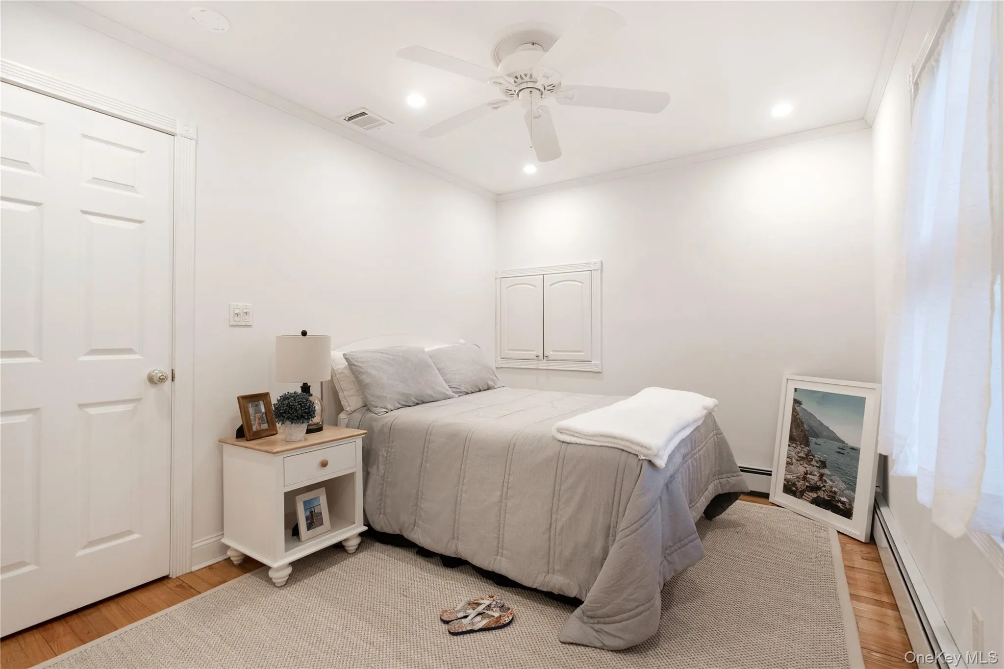 Bedroom featuring light wood-type flooring, visible vents, ornamental molding, and baseboard heating Bedroom featuring light wood-type flooring, visible vents, ornamental molding, and baseboard heating