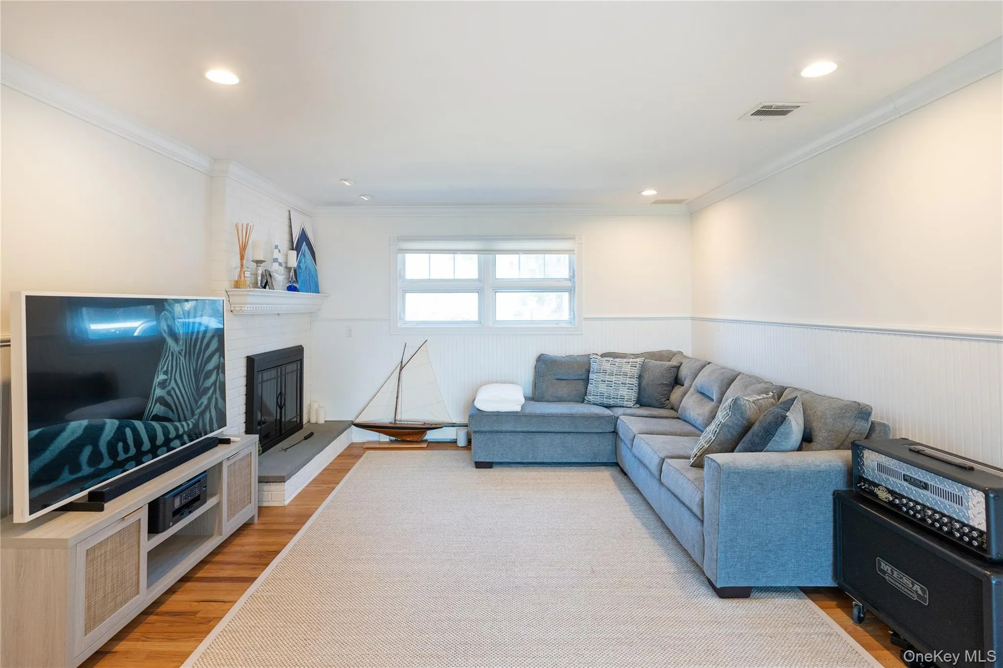 Living room featuring a brick fireplace, recessed lighting, ornamental molding, visible vents, and light wood-style flooring Living room featuring a brick fireplace, recessed lighting, ornamental molding, visible vents, and light wood-style flooring