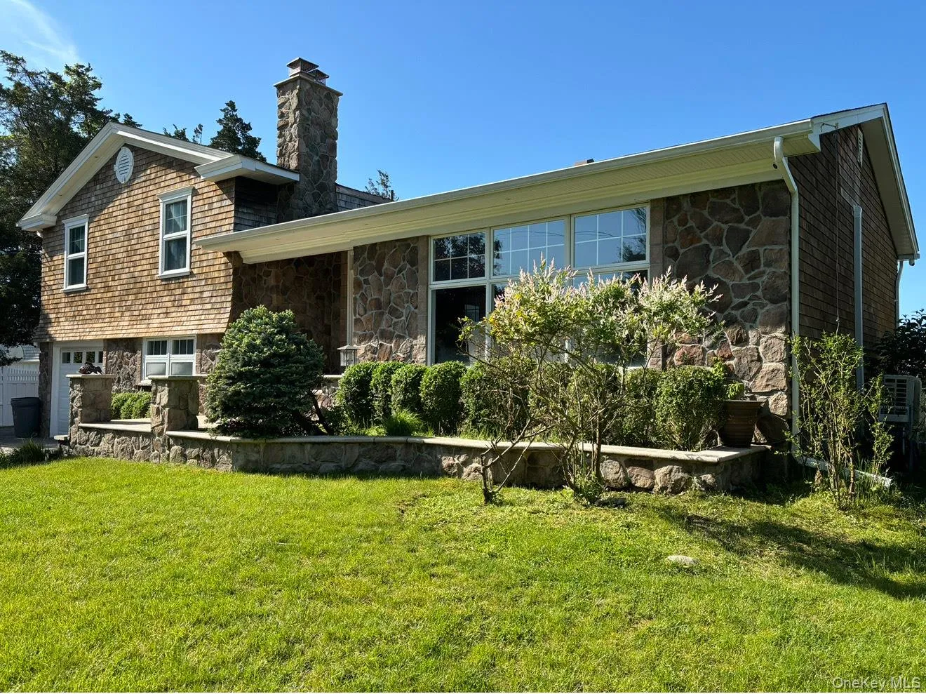 Tri-level home featuring a front yard, stone siding, a chimney, and an attached garage Tri-level home featuring a front yard, stone siding, a chimney, and an attached garage