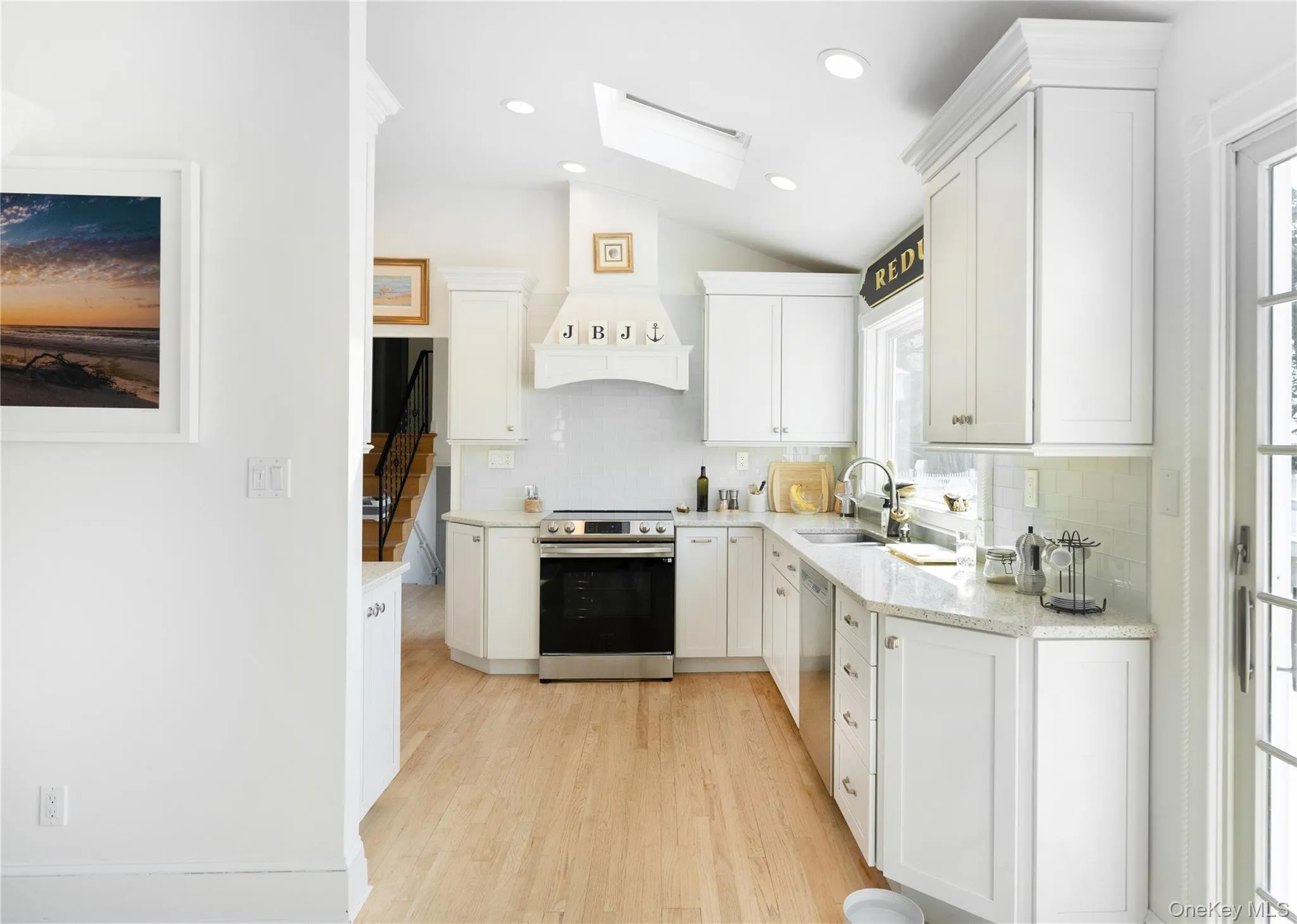 Kitchen featuring white cabinets, light wood finished floors, appliances with stainless steel finishes, a sink, and lofted ceiling with skylight Kitchen featuring white cabinets, light wood finished floors, appliances with stainless steel finishes, a sink, and lofted ceiling with skylight