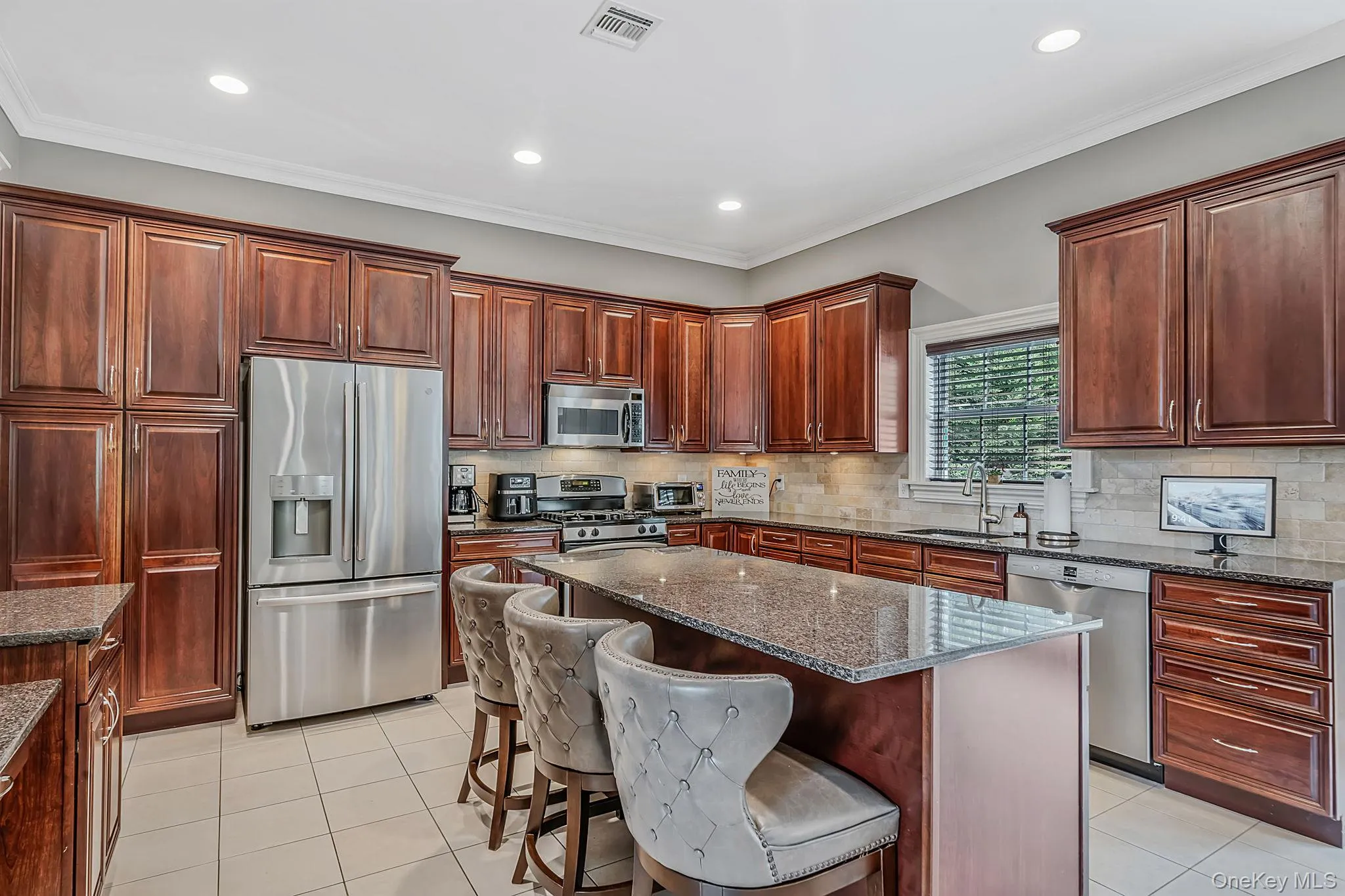 Kitchen featuring extensive wood cabinetry, stainless steel appliances, a large center island with a granite countertop, and tile flooring Kitchen featuring extensive wood cabinetry, stainless steel appliances, a large center island with a granite countertop, and tile flooring