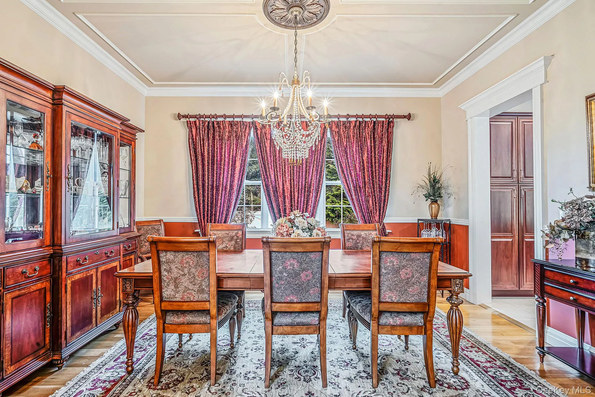 Tray ceiling with crown molding, crystal chandelier, wood-finish flooring and an arched doorway Tray ceiling with crown molding, crystal chandelier, wood-finish flooring and an arched doorway