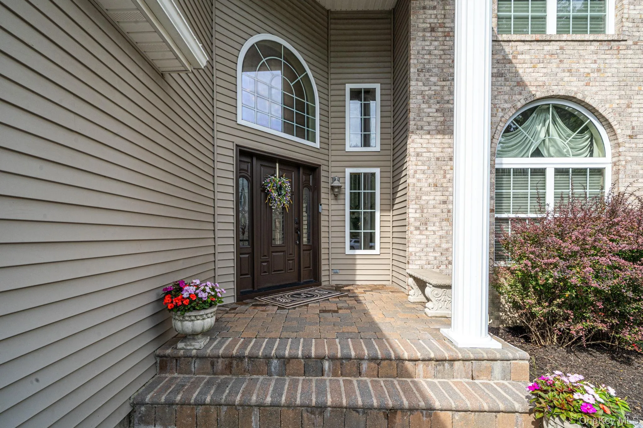 Brick and siding exterior featuring a decorative arched window, brick paver steps, and a fluted column Brick and siding exterior featuring a decorative arched window, brick paver steps, and a fluted column