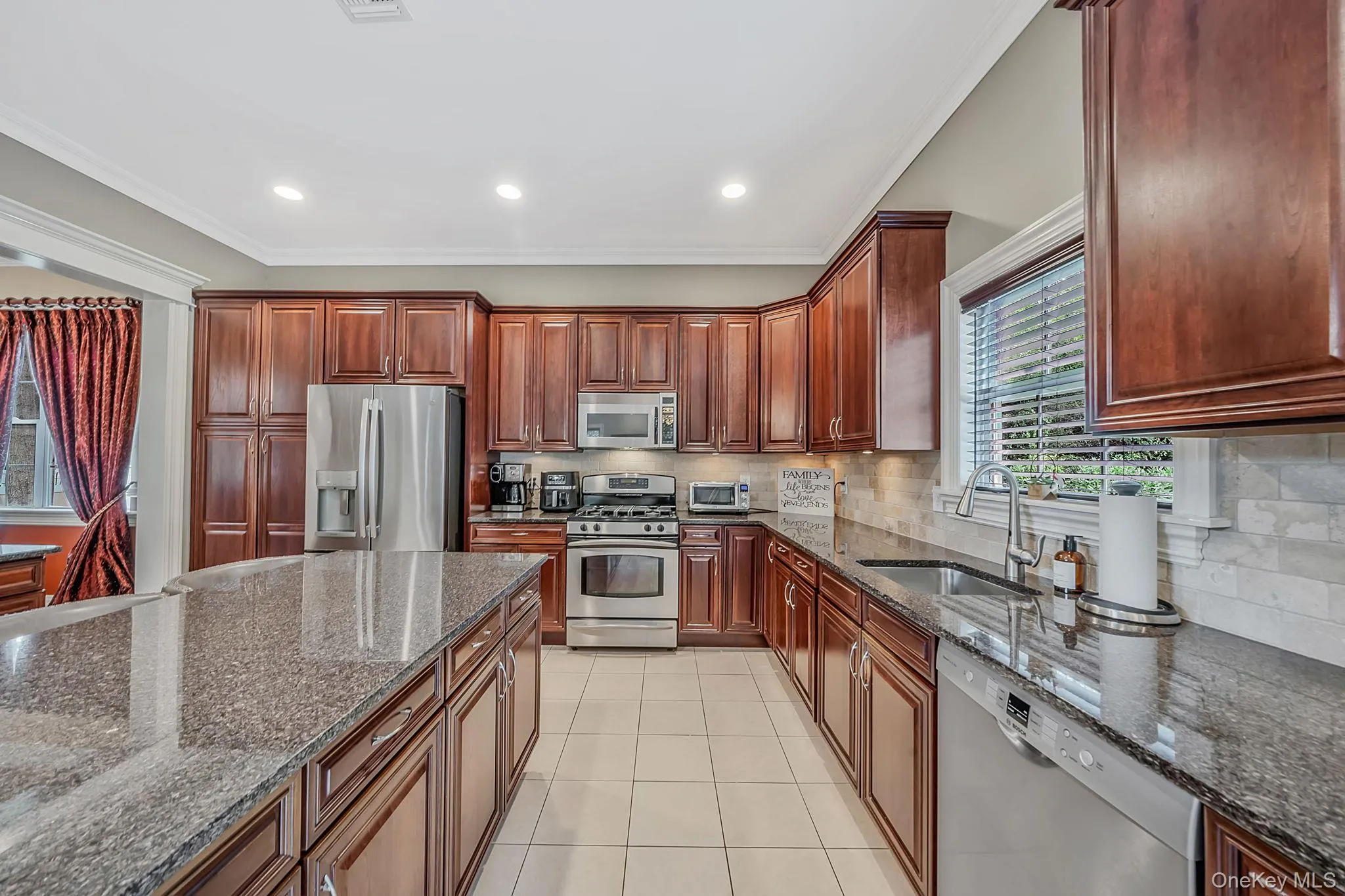 Gourmet kitchen featuring a large central island, dark wood cabinetry, stainless steel appliances, granite countertops, and a tiled backsplash Gourmet kitchen featuring a large central island, dark wood cabinetry, stainless steel appliances, granite countertops, and a tiled backsplash