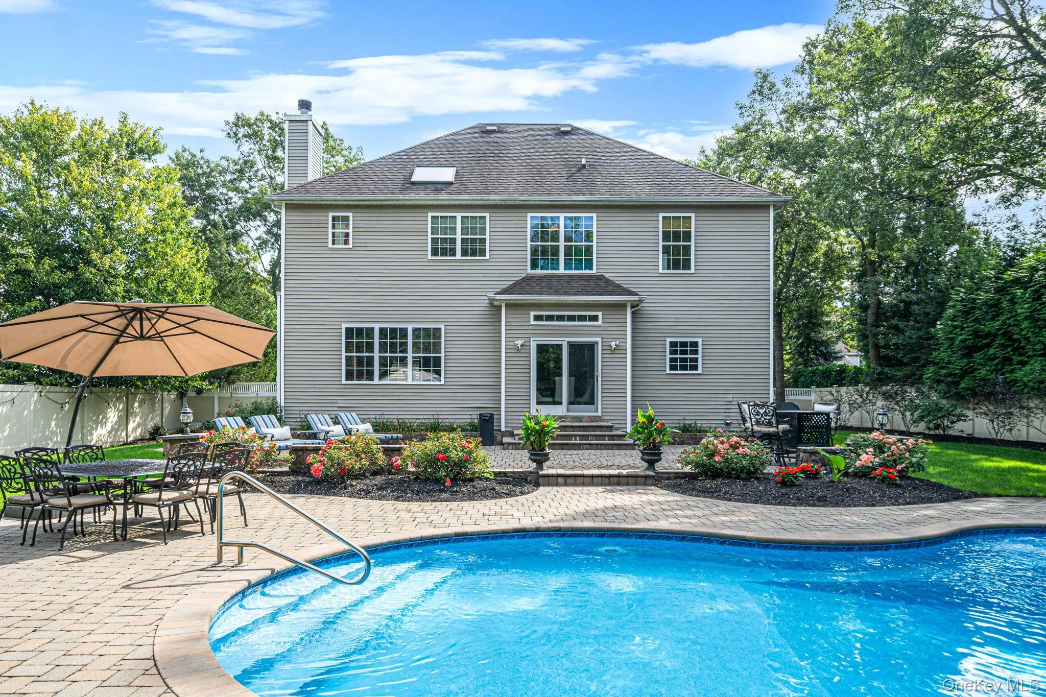 Expansive paver patio featuring a built-in pool, lush landscaping, and a direct entry to the home Expansive paver patio featuring a built-in pool, lush landscaping, and a direct entry to the home