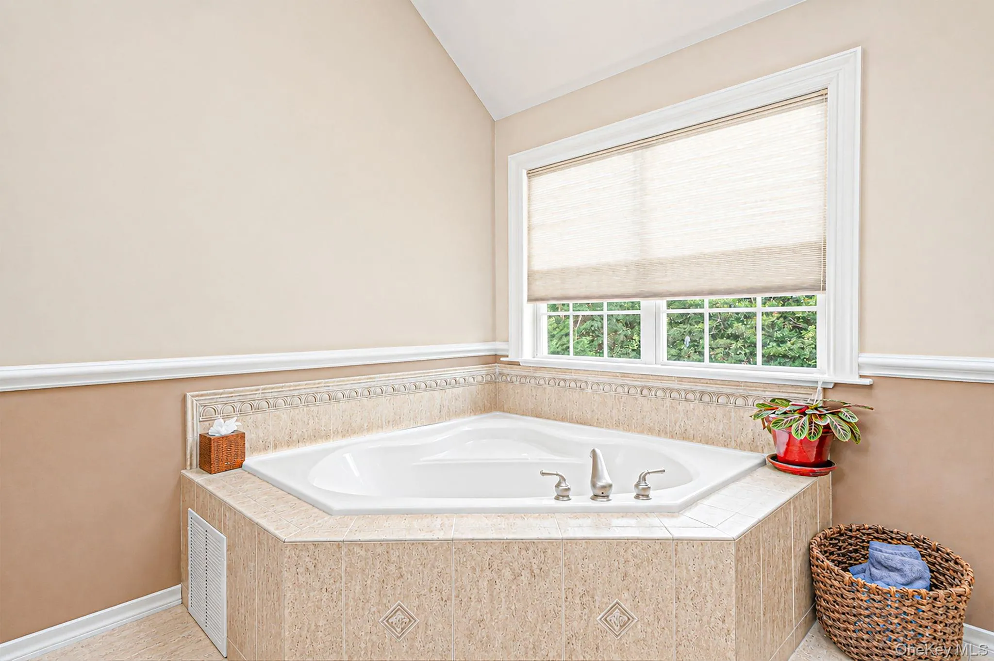 Corner soaking tub with tiled surround, polished chrome fixtures, and a white framed window Corner soaking tub with tiled surround, polished chrome fixtures, and a white framed window
