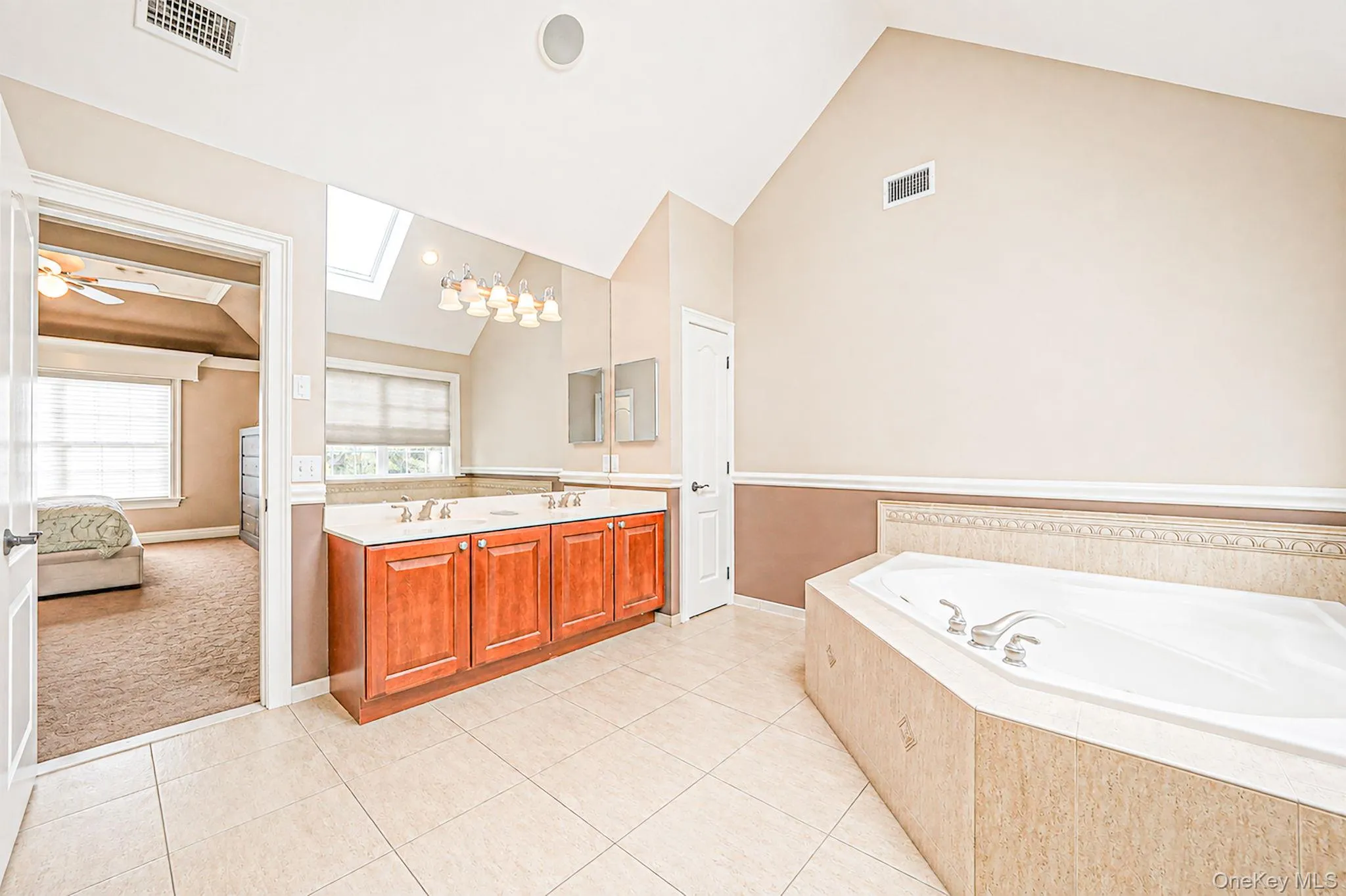 Vaulted ceiling, skylight, dual vanity with wood cabinetry, drop-in soaking tub, and tile flooring Vaulted ceiling, skylight, dual vanity with wood cabinetry, drop-in soaking tub, and tile flooring