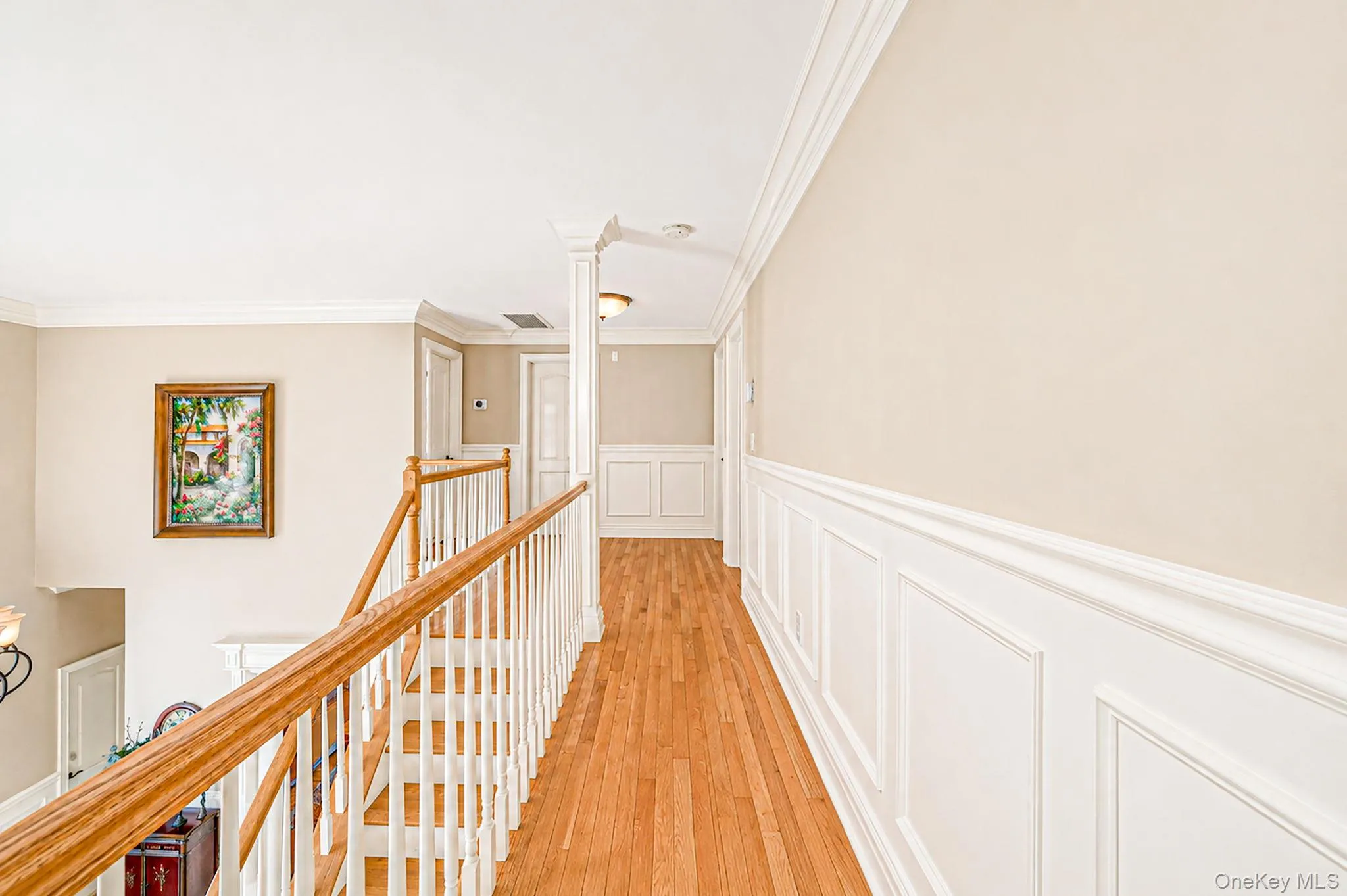 Hardwood flooring, white wainscoting, crown molding, paneled doors, and a wood banister Hardwood flooring, white wainscoting, crown molding, paneled doors, and a wood banister