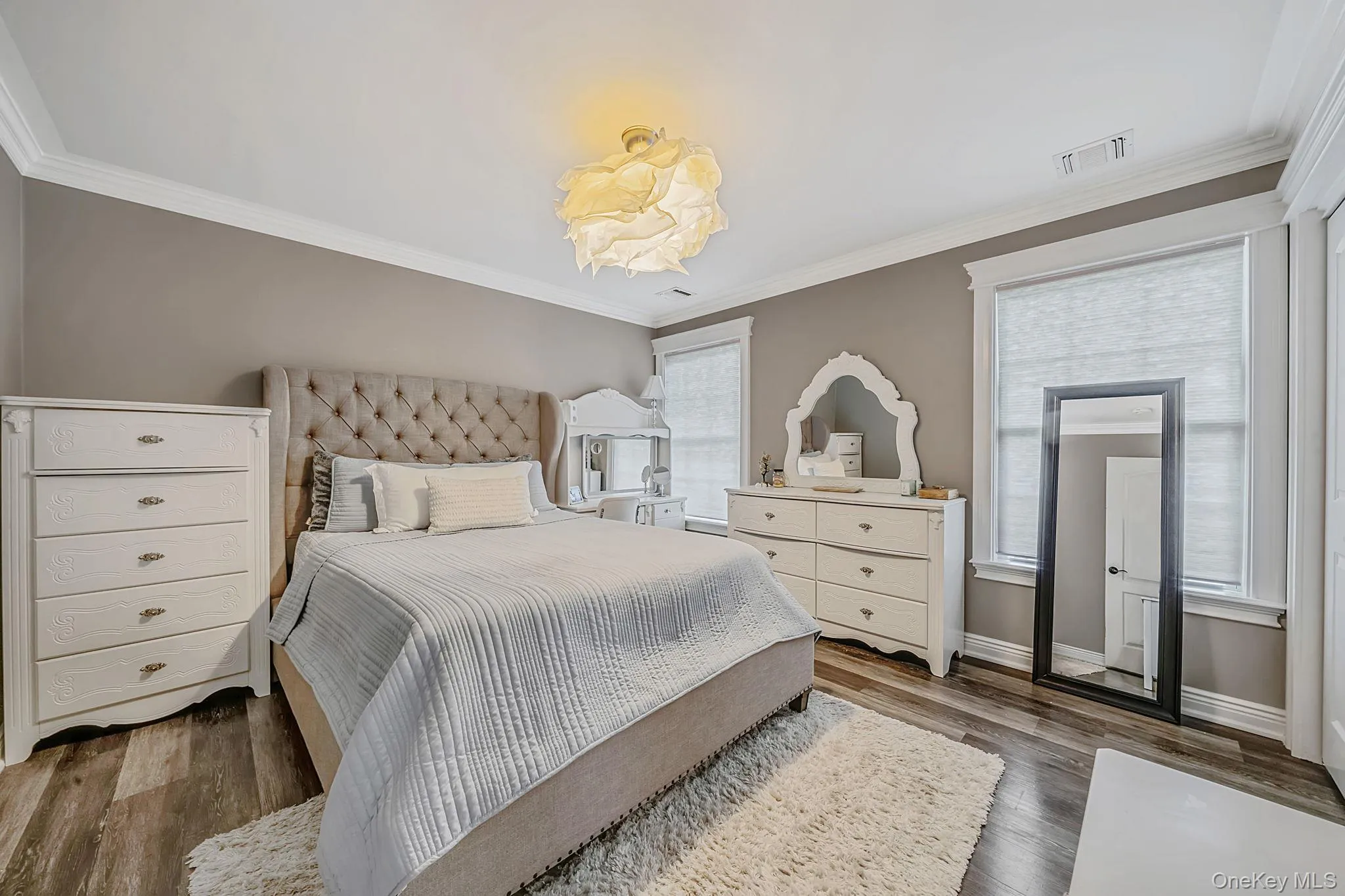 Crown molding detail, wood-finish flooring, two windows with roller shades, and a ceiling-mounted light fixture Crown molding detail, wood-finish flooring, two windows with roller shades, and a ceiling-mounted light fixture