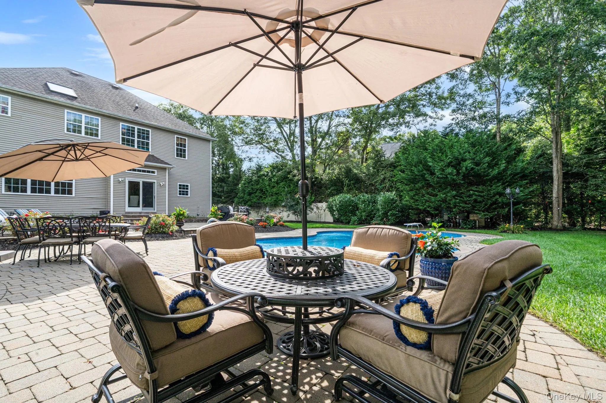 Expansive paver patio with multiple seating areas, a sparkling in-ground pool, and a backdrop of mature trees Expansive paver patio with multiple seating areas, a sparkling in-ground pool, and a backdrop of mature trees