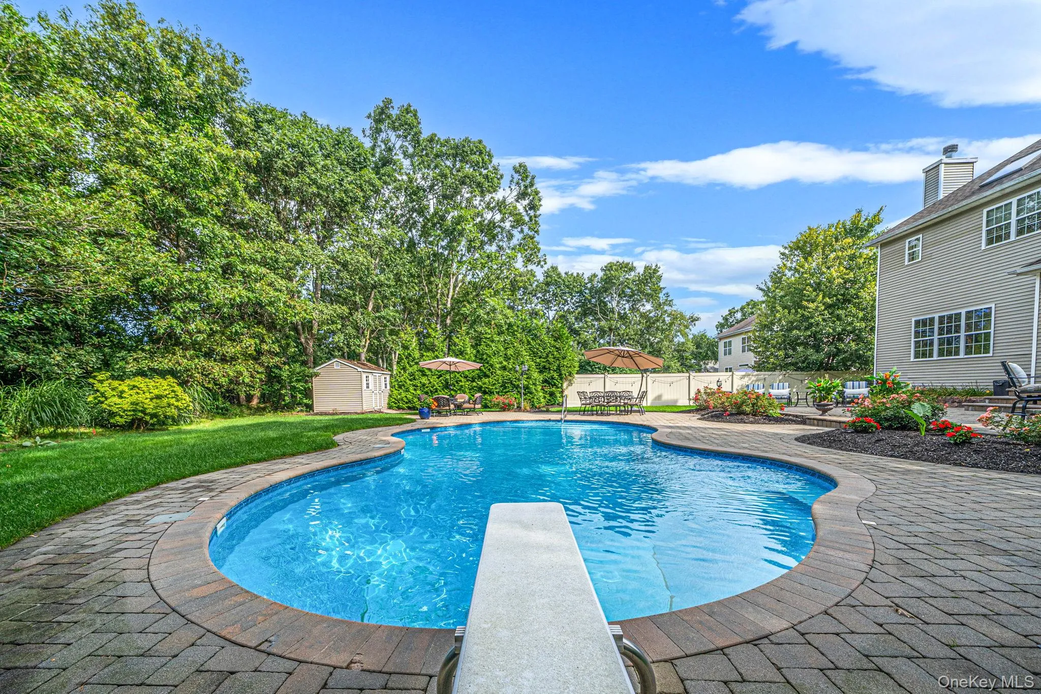 Freeform swimming pool with a diving board, paver surround, and mature landscaping Freeform swimming pool with a diving board, paver surround, and mature landscaping