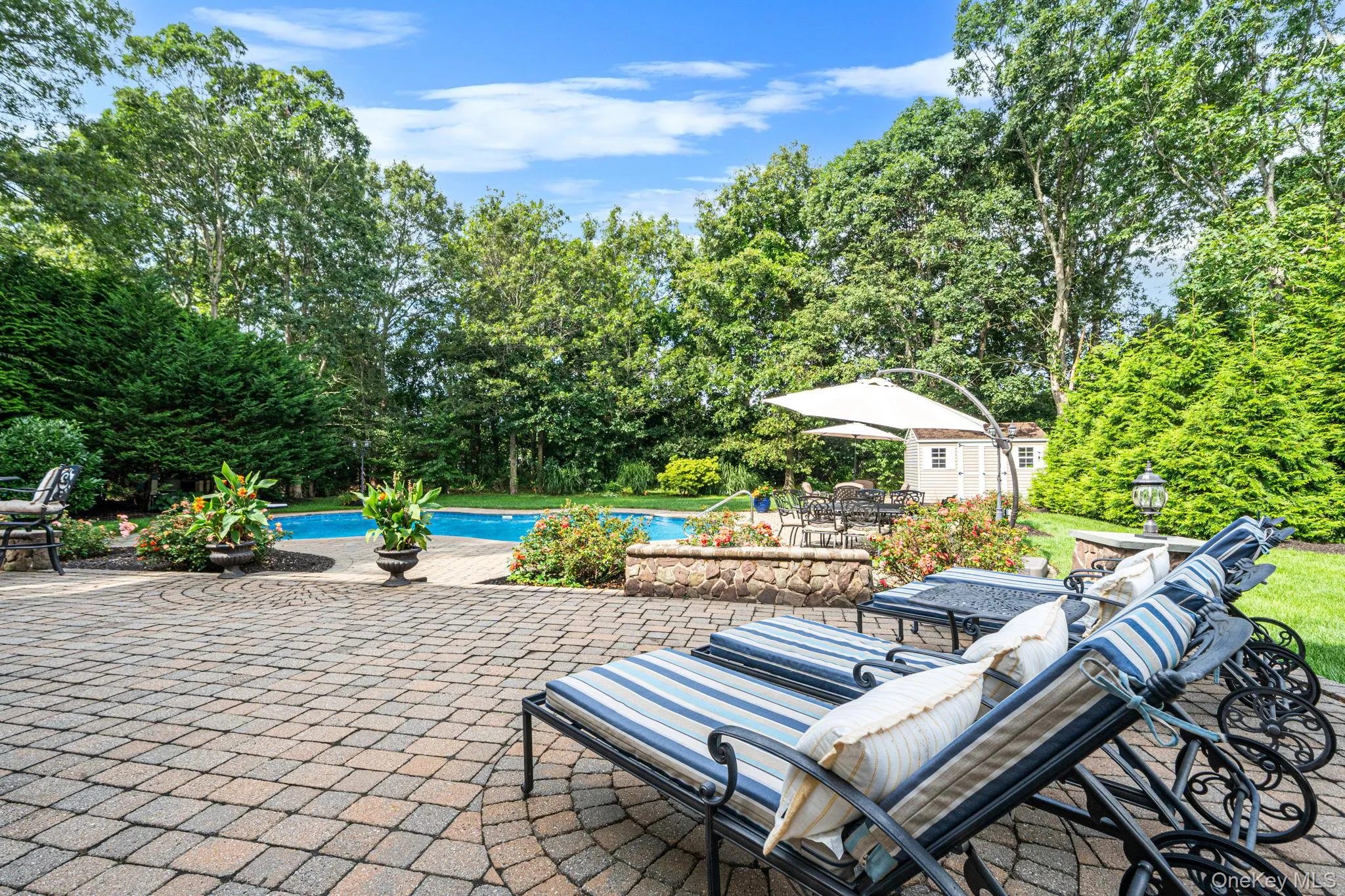 Expansive paver patio with an in-ground swimming pool, and lush perimeter landscaping Expansive paver patio with an in-ground swimming pool, and lush perimeter landscaping
