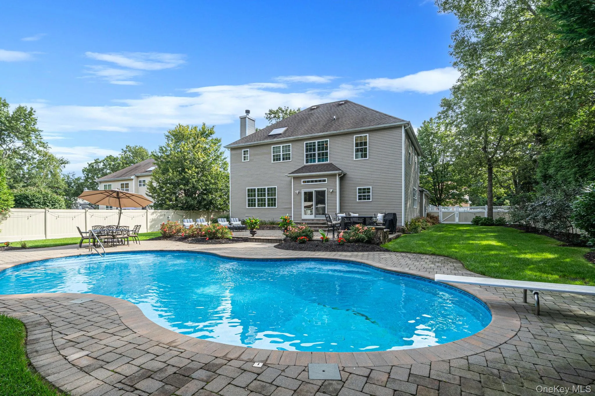 Fenced backyard featuring a large in-ground pool with a diving board, paver surround, and adjacent patio area Fenced backyard featuring a large in-ground pool with a diving board, paver surround, and adjacent patio area