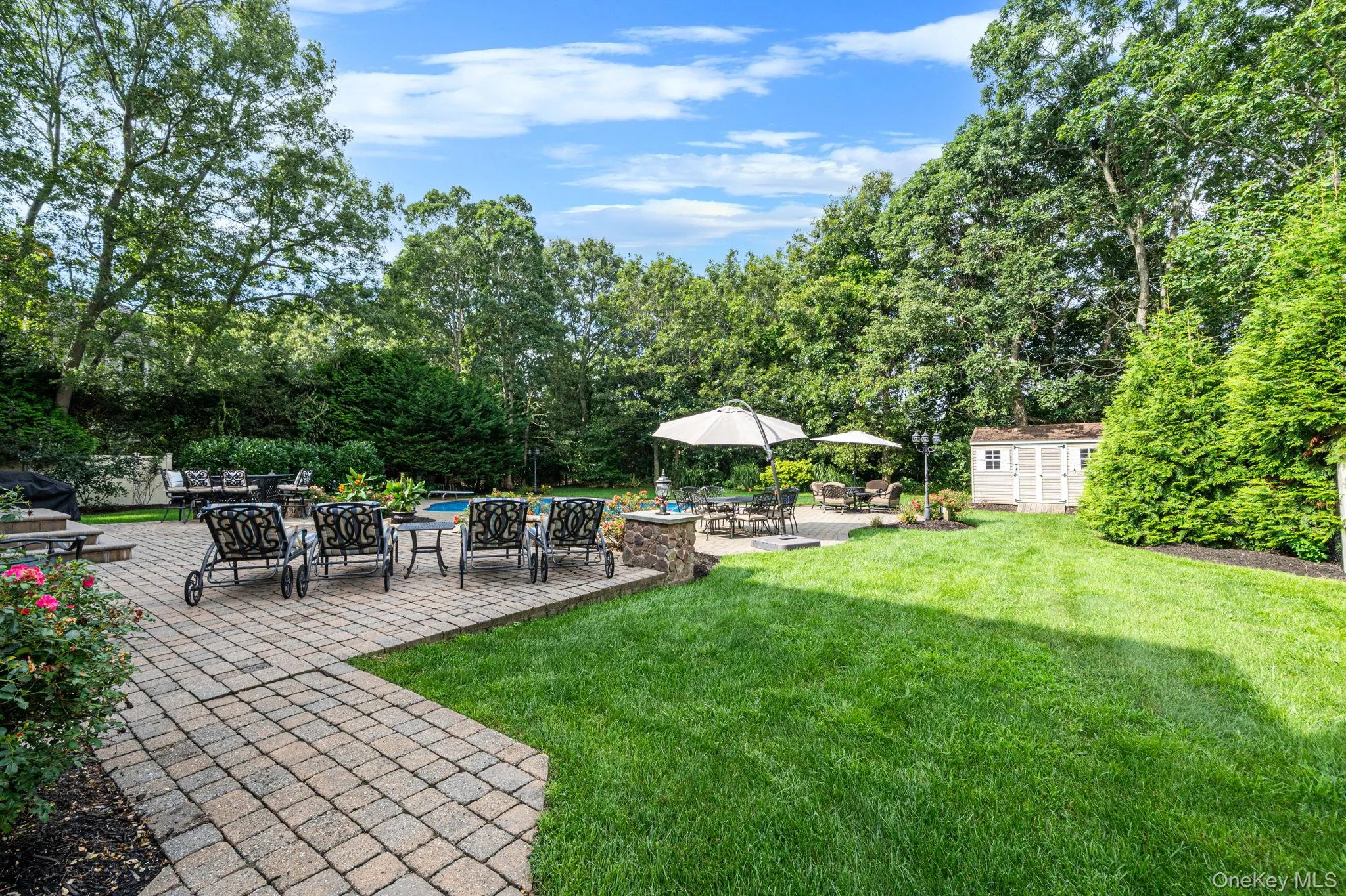 Expansive backyard featuring a manicured lawn, paver patio, in-ground pool, and mature trees Expansive backyard featuring a manicured lawn, paver patio, in-ground pool, and mature trees