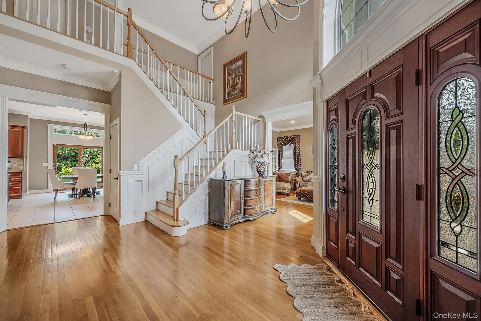 Two-story foyer featuring wood-finish flooring, a grand staircase with white balusters, and a dark wood front door with stained glass panels. Two-story foyer featuring wood-finish flooring, a grand staircase with white balusters, and a dark wood front door with stained glass panels.