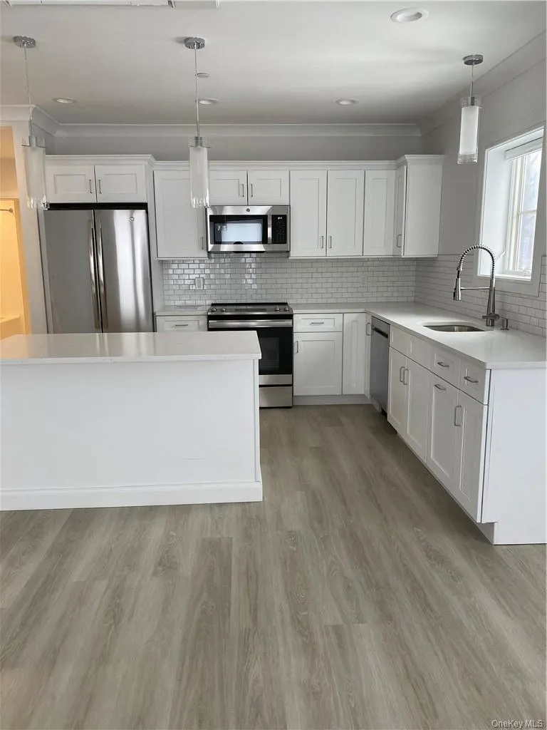 Kitchen featuring backsplash, hanging light fixtures, appliances with stainless steel finishes, and light hardwood / wood-style flooring Kitchen featuring backsplash, hanging light fixtures, appliances with stainless steel finishes, and light hardwood / wood-style flooring