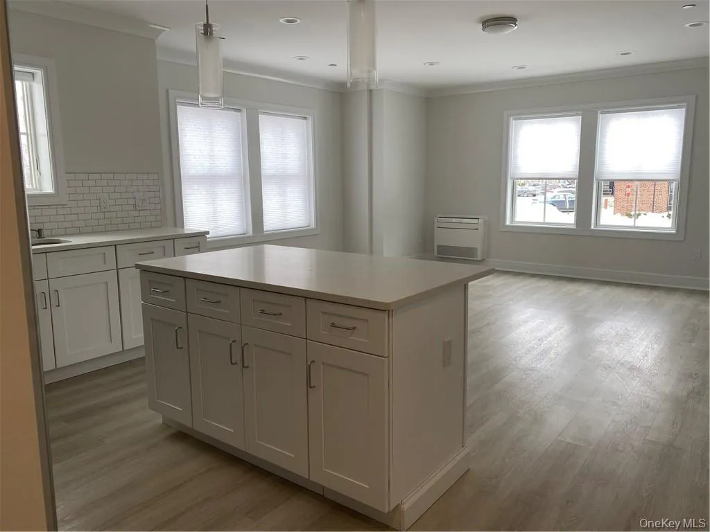 Kitchen featuring white cabinetry, crown molding, a center island, light hardwood / wood-style floors, and decorative backsplash Kitchen featuring white cabinetry, crown molding, a center island, light hardwood / wood-style floors, and decorative backsplash