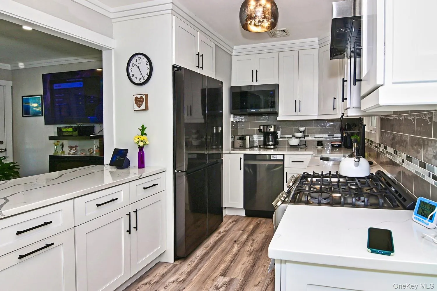 White cabinetry with matte black hardware, integrated stainless steel appliances, wood-finish flooring, and a stone-finish countertop