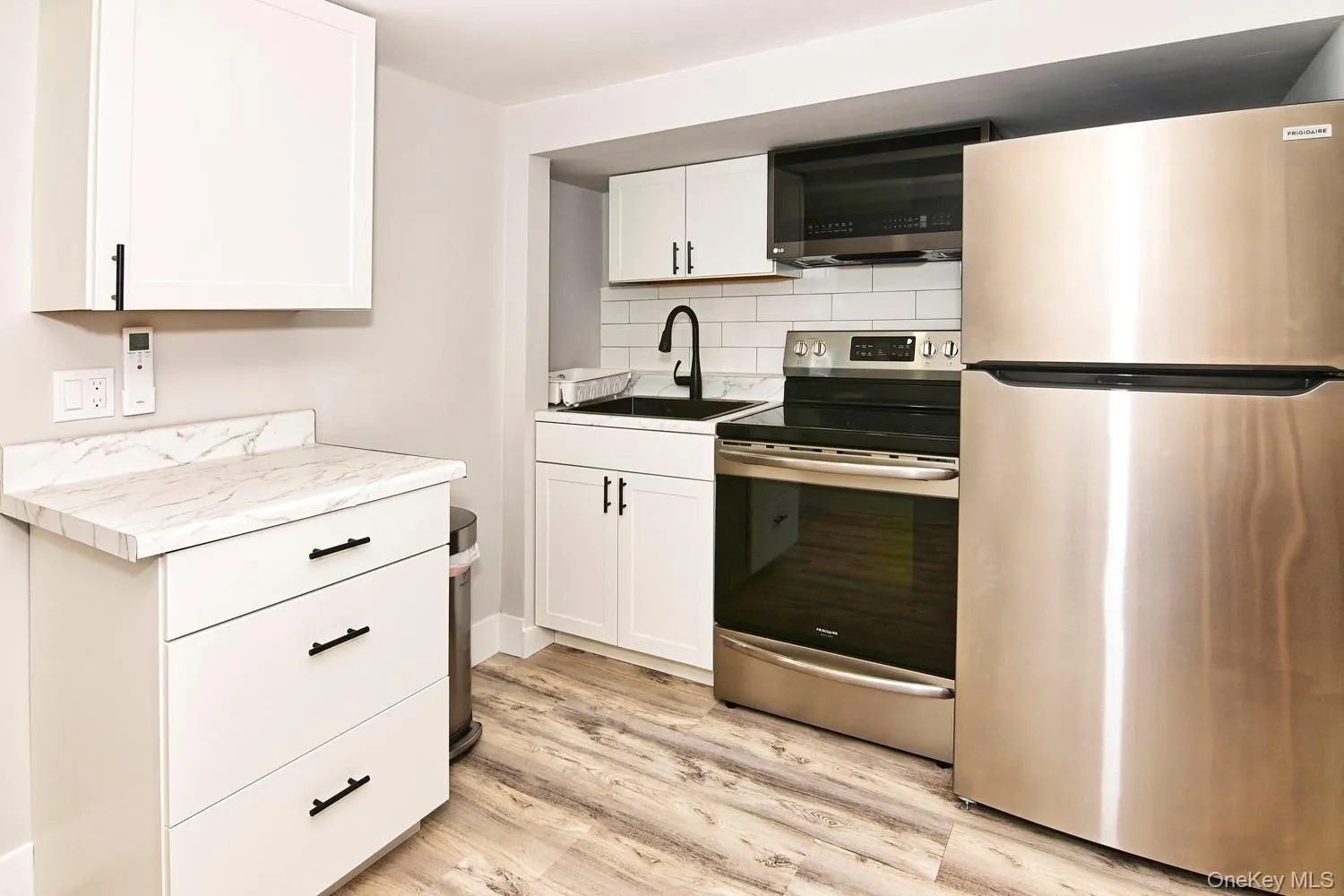 White cabinetry with matte black hardware, wood-finish flooring, white subway tile backsplash, stainless steel appliances, and a black sink with a matte black faucet