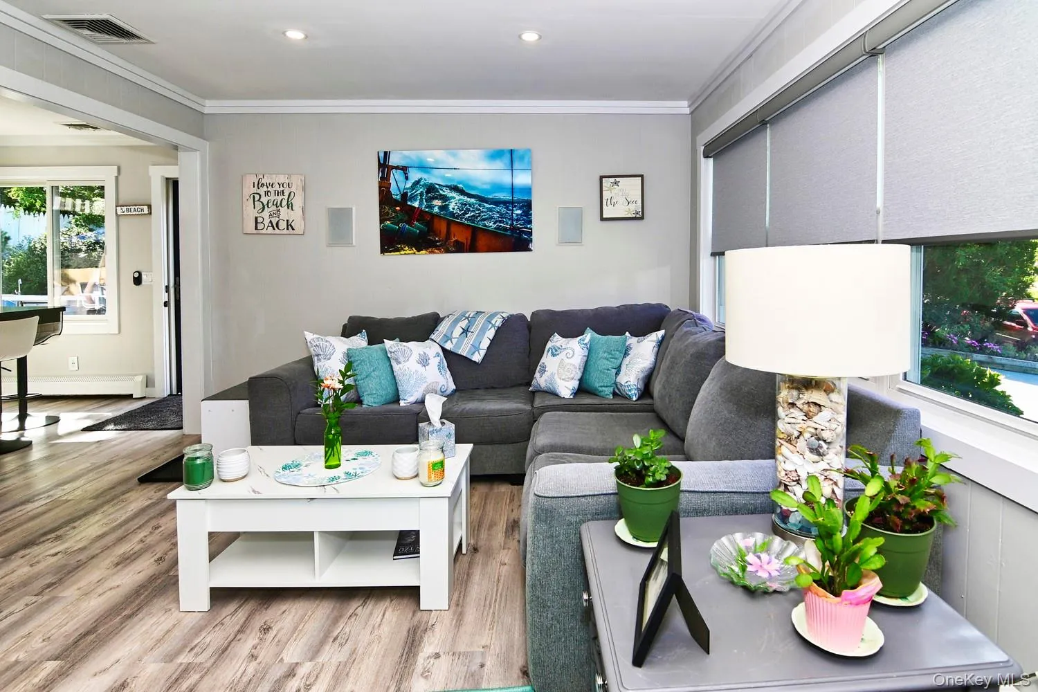 Open-concept living area featuring a sectional seating arrangement, wood-finish flooring throughout, recessed ceiling lighting, and large windows with cellular shade treatments