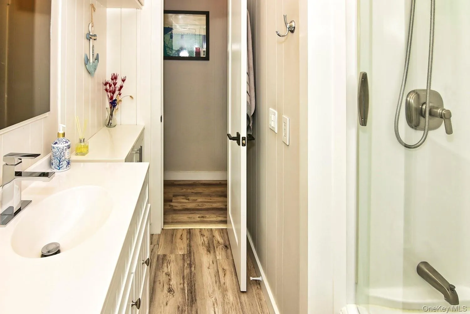 White vanity with an integrated sink and chrome faucet, white shiplap wall paneling, wood-finish flooring, and a shower with brushed nickel fixtures
