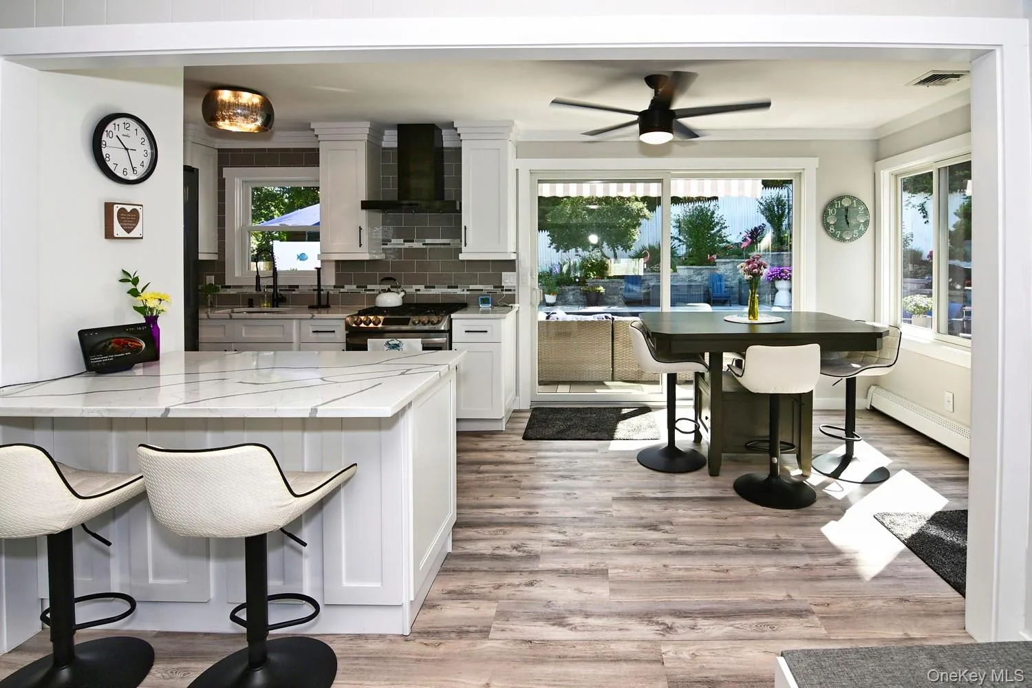 Open-concept kitchen and dining area featuring white cabinetry, stainless steel appliances, quartz countertops, waterfall island, wood-finish flooring, and expansive glass sliding doors overlooking the outdoor space