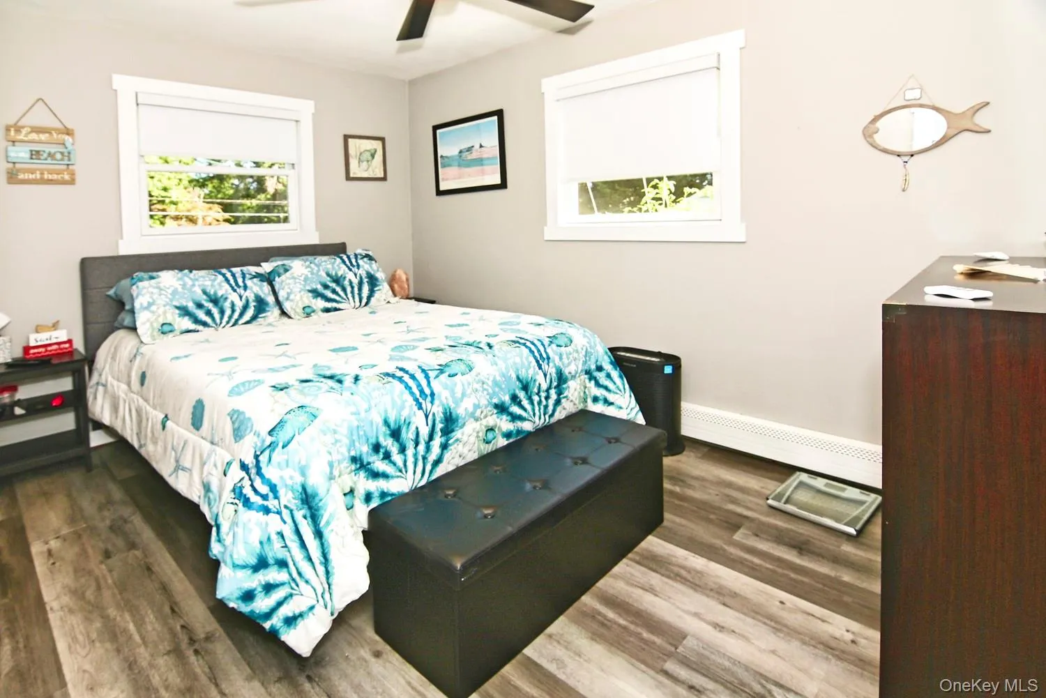 Bright corner bedroom with dual windows flooding the space with natural light, wood-finish flooring throughout, and a ceiling fan
