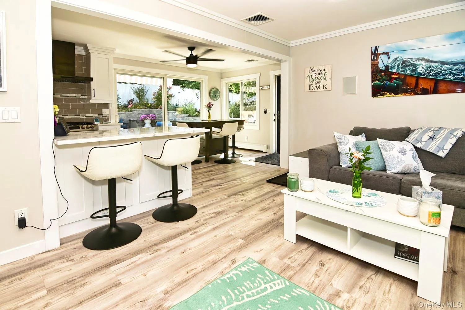 Wood-finish flooring, white kitchen cabinetry, subway tile backsplash, sliding glass door, and crown molding