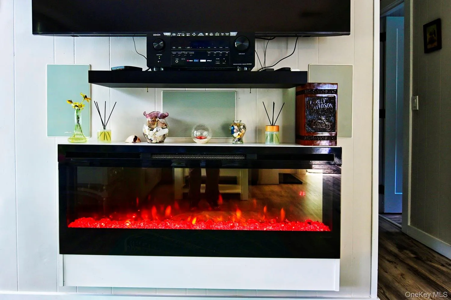 Modern entertainment wall featuring a wall-mounted flat-screen television, built-in electric fireplace with realistic flame effect, and floating shelving with glass display surfaces