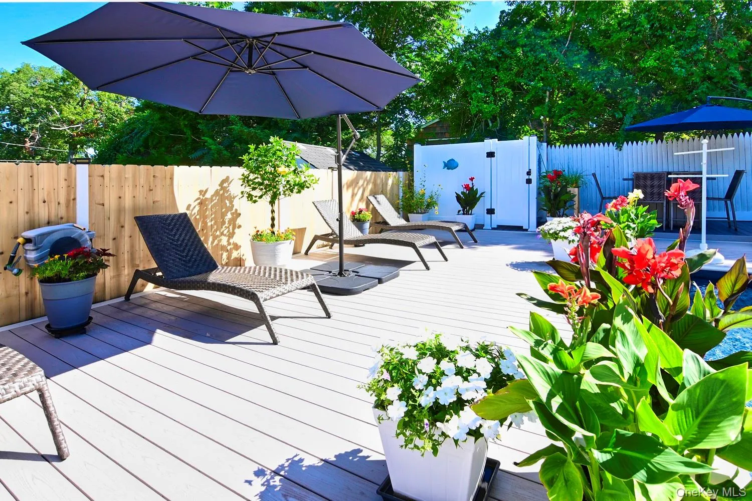 Expansive composite deck with white finish providing multiple entertaining zones, anchored by a dark umbrella and lounge seating