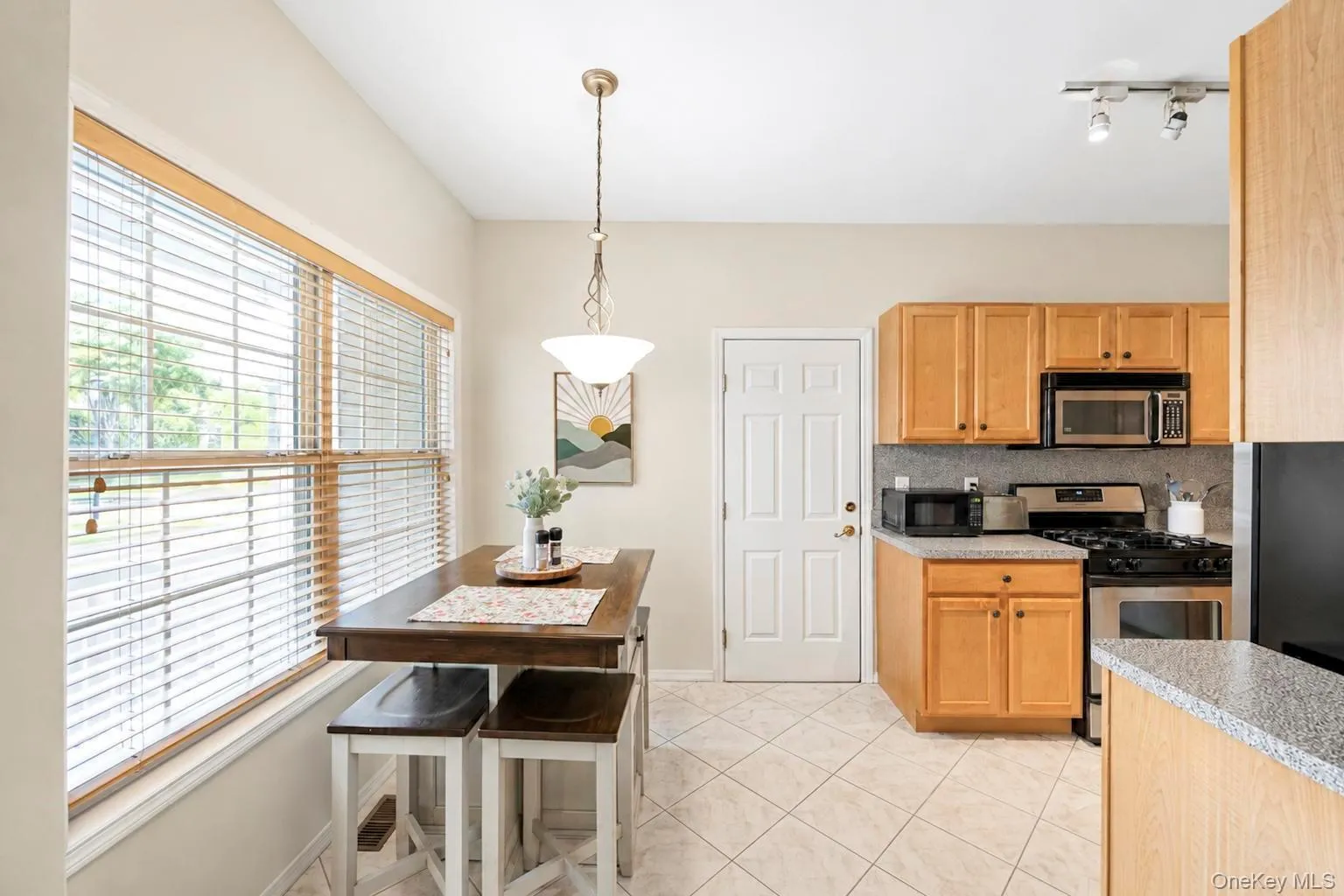 Eat in Kitchen featuring light wood cabinetry, stainless steel appliances, tiled flooring, and a large window with blinds Eat in Kitchen featuring light wood cabinetry, stainless steel appliances, tiled flooring, and a large window with blinds