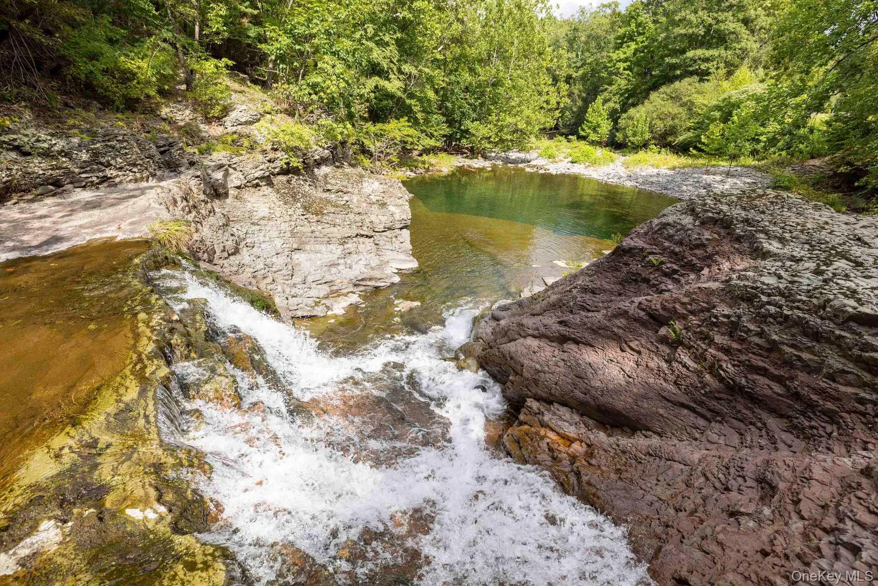Natural rock formations create a secluded waterfall and swimming hole surrounded by woodland. Natural rock formations create a secluded waterfall and swimming hole surrounded by woodland.