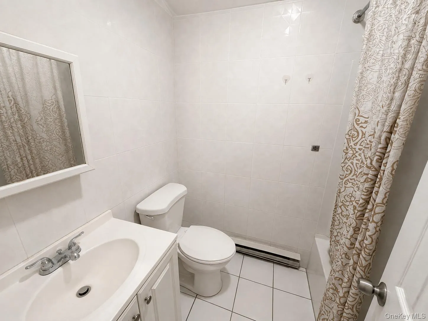 White tiled bathroom with a vanity sink, mirror, and toilet White tiled bathroom with a vanity sink, mirror, and toilet