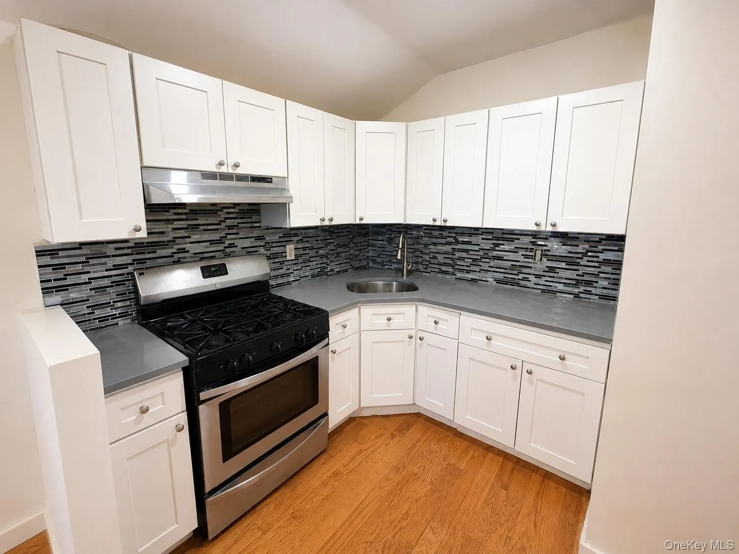 Full kitchen with white shaker cabinetry, stainless steel range, stainless steel range hood, stone-finish countertops, and mosaic tile backsplash Full kitchen with white shaker cabinetry, stainless steel range, stainless steel range hood, stone-finish countertops, and mosaic tile backsplash
