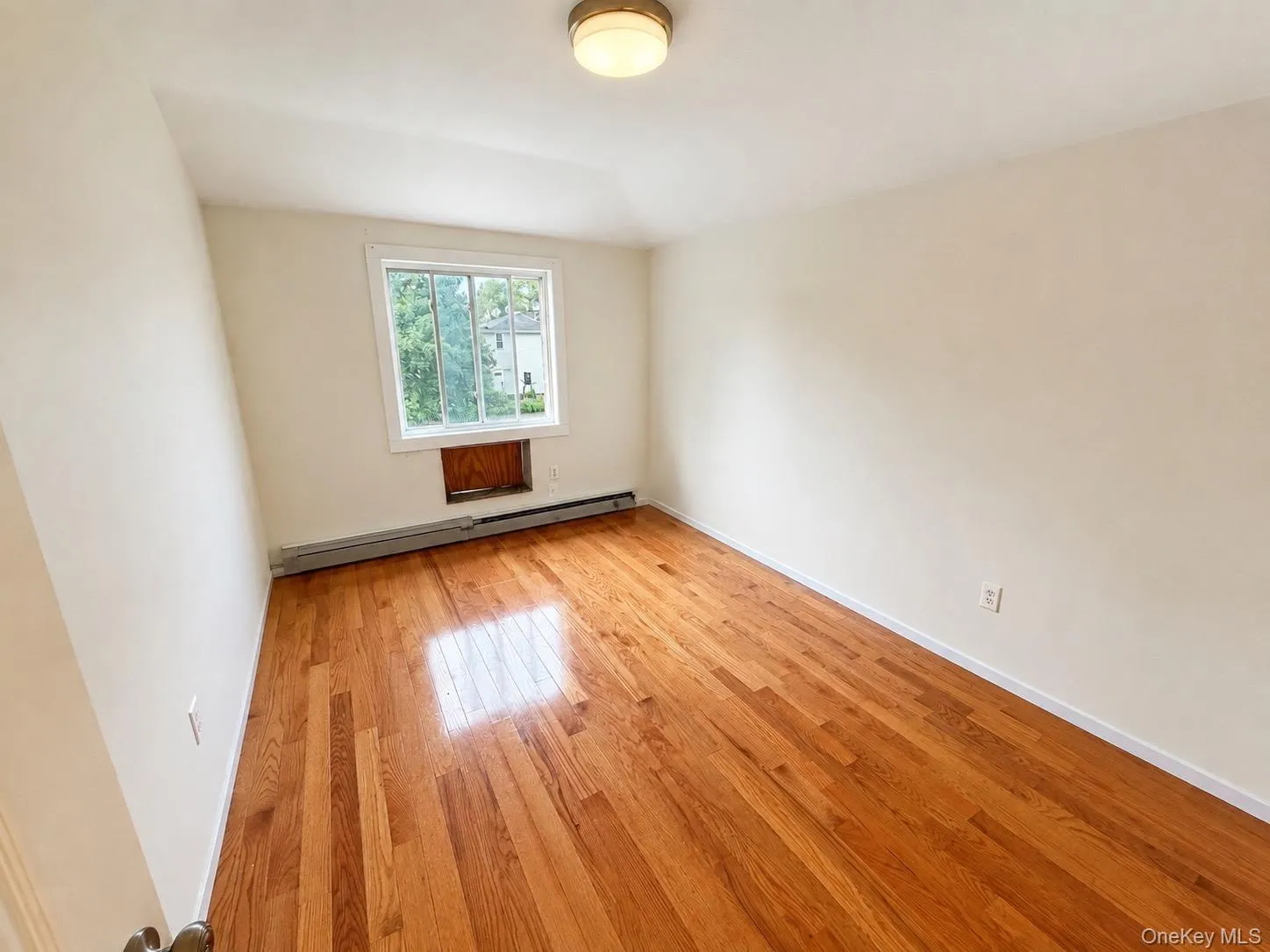 Hardwood flooring, neutral wall tones, flush mount ceiling light fixture, and a window with white trim Hardwood flooring, neutral wall tones, flush mount ceiling light fixture, and a window with white trim
