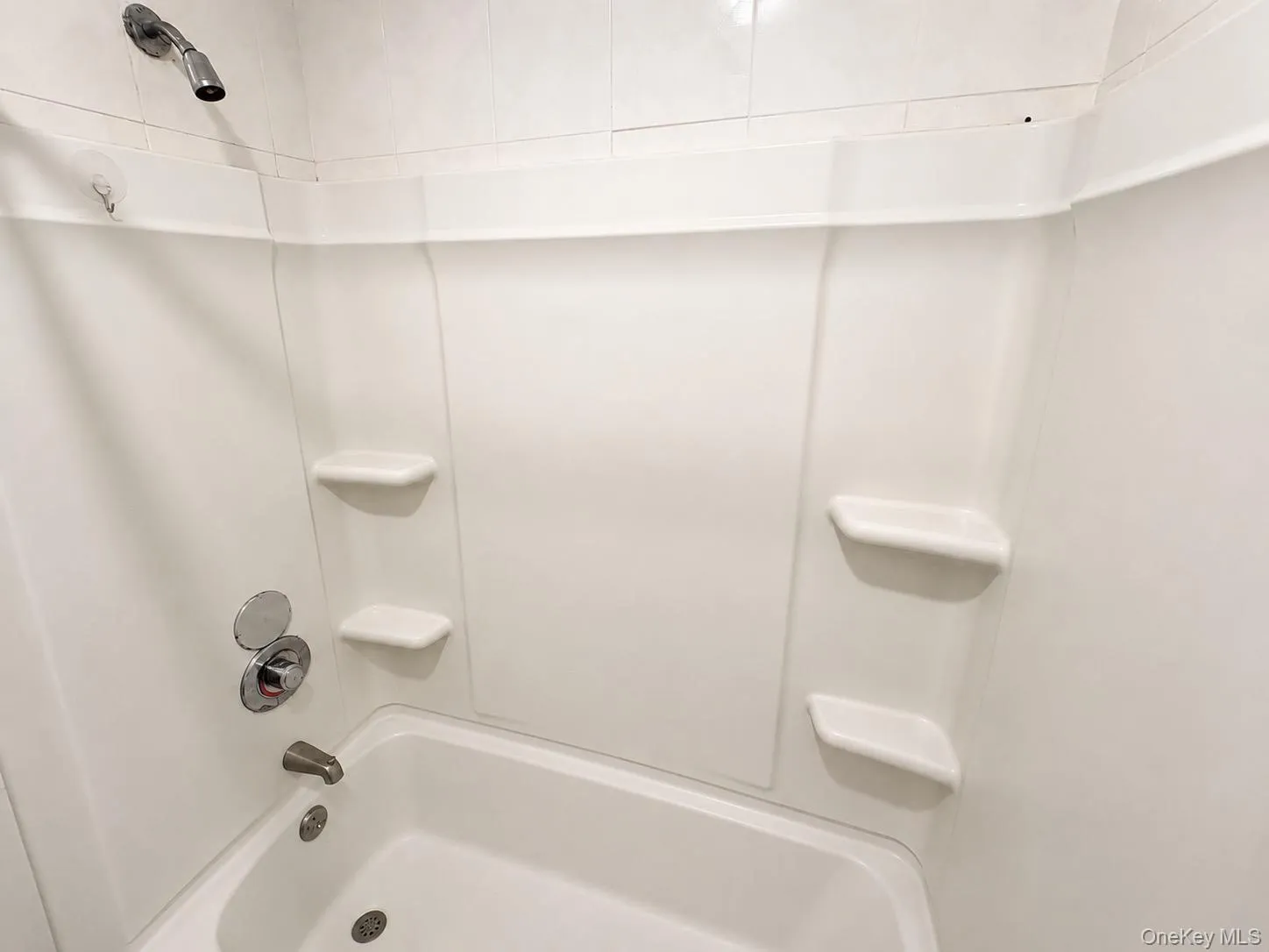 White bathtub with integrated shelving, chrome fixtures, and a tiled shower surround White bathtub with integrated shelving, chrome fixtures, and a tiled shower surround