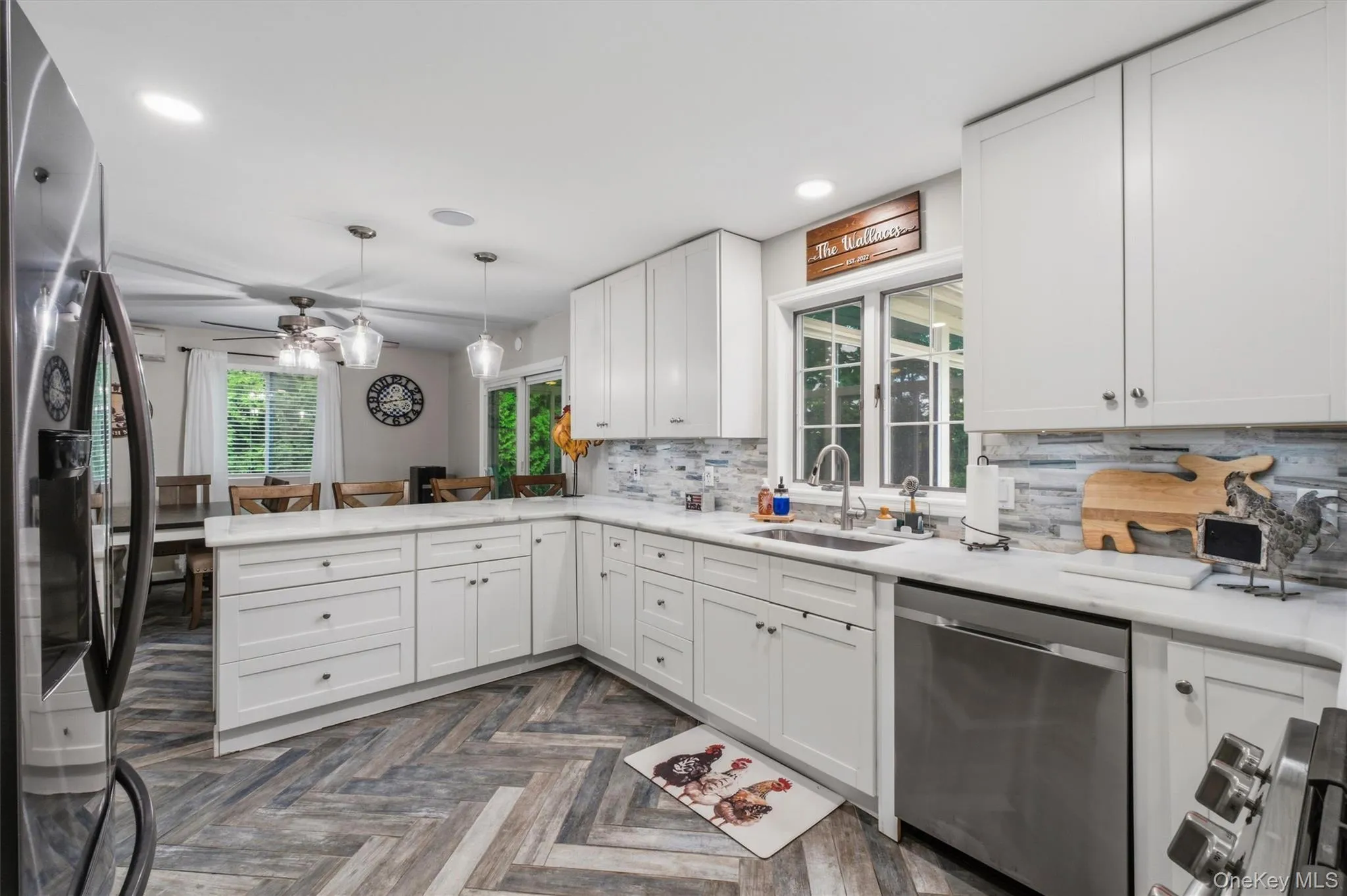 White cabinetry with modern hardware, stainless steel appliances, light-toned stone countertops, tile backsplash, and wood-finish flooring in a herringbone pattern White cabinetry with modern hardware, stainless steel appliances, light-toned stone countertops, tile backsplash, and wood-finish flooring in a herringbone pattern