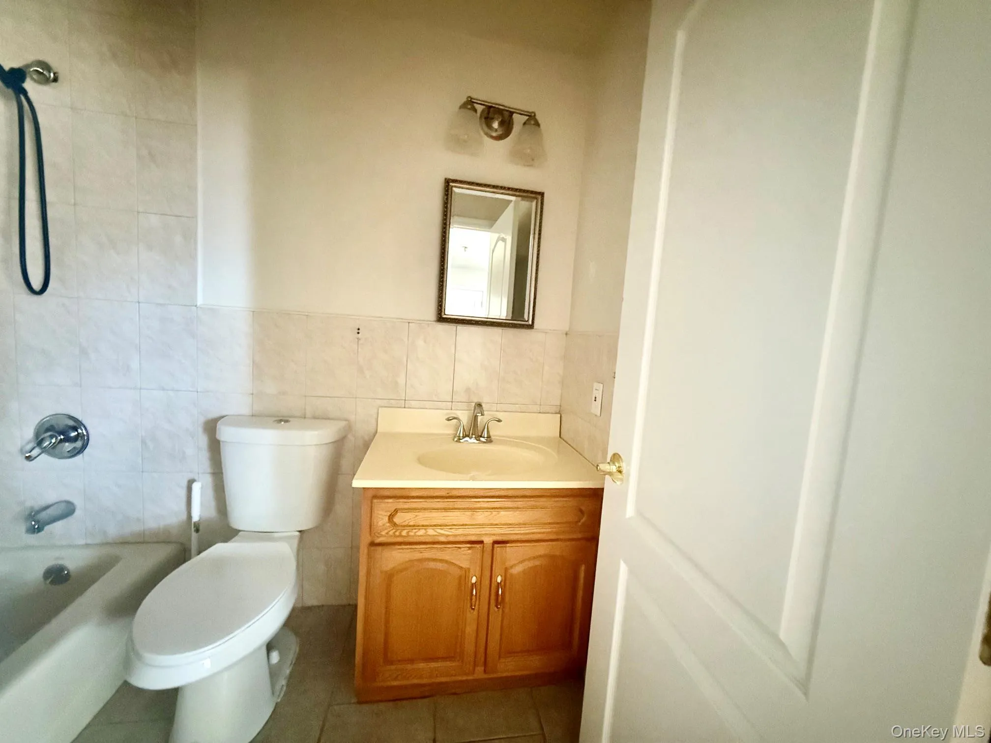 Bathroom featuring a wood-finish vanity with an integrated sink, a wall-mounted mirror, and a tiled shower/tub combination Bathroom featuring a wood-finish vanity with an integrated sink, a wall-mounted mirror, and a tiled shower/tub combination