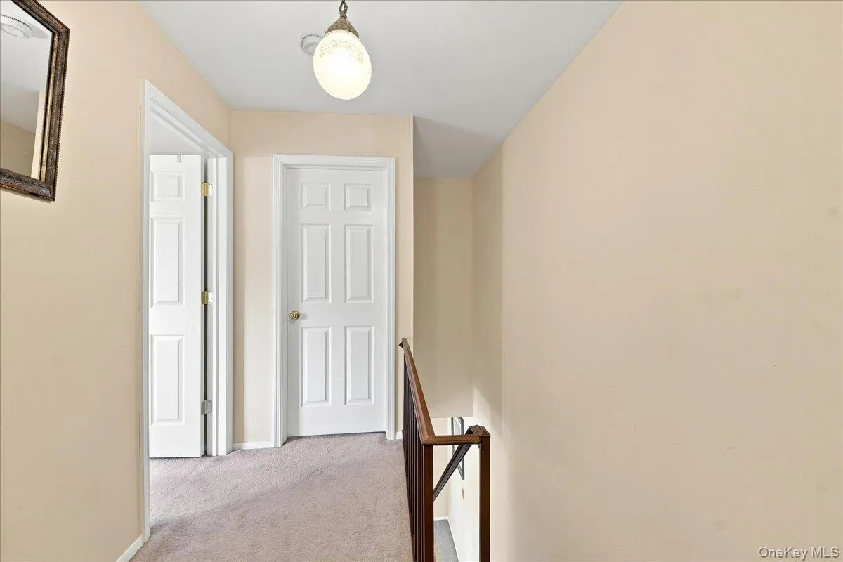 Carpeted hallway with painted walls, white paneled doors, and a decorative ceiling light fixture Carpeted hallway with painted walls, white paneled doors, and a decorative ceiling light fixture