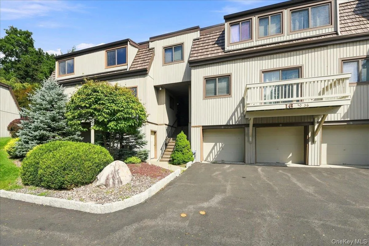 Multi-level dwelling with vertical siding, multiple dormer windows, a private balcony, and integrated garage bays with overhead doors Multi-level dwelling with vertical siding, multiple dormer windows, a private balcony, and integrated garage bays with overhead doors