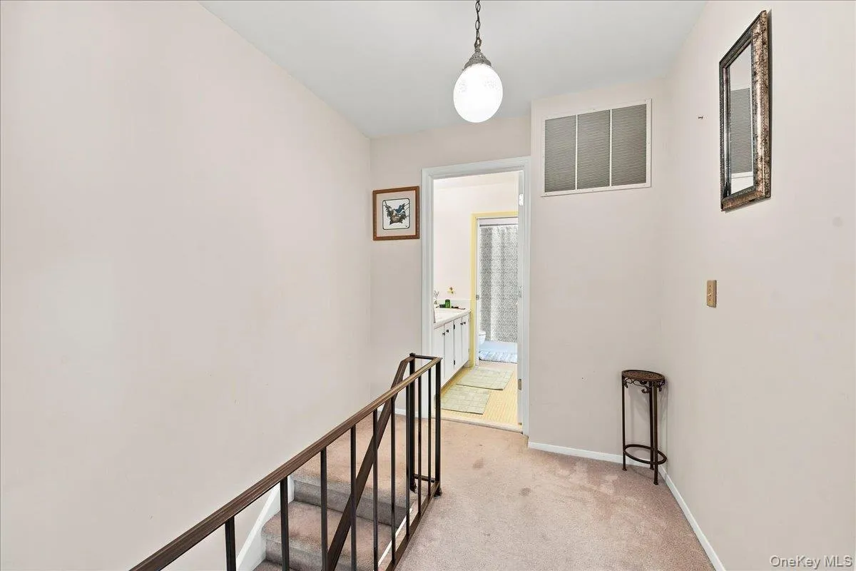 Carpeted hallway with a metal stair railing, an overhead globe light fixture, and an internal window Carpeted hallway with a metal stair railing, an overhead globe light fixture, and an internal window