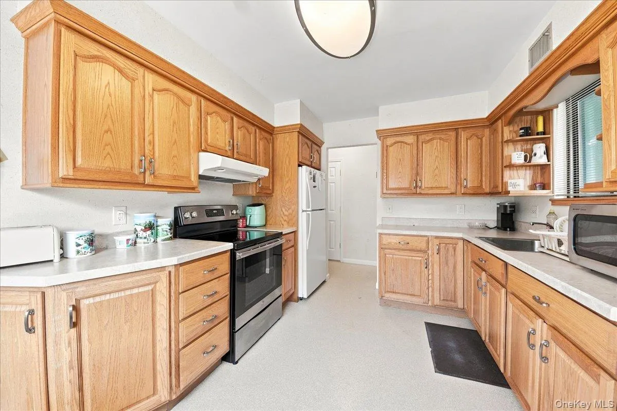 Kitchen featuring wood-finish cabinetry, light-toned countertops, and a full suite of appliances including a refrigerator, range, and built-in microwave Kitchen featuring wood-finish cabinetry, light-toned countertops, and a full suite of appliances including a refrigerator, range, and built-in microwave