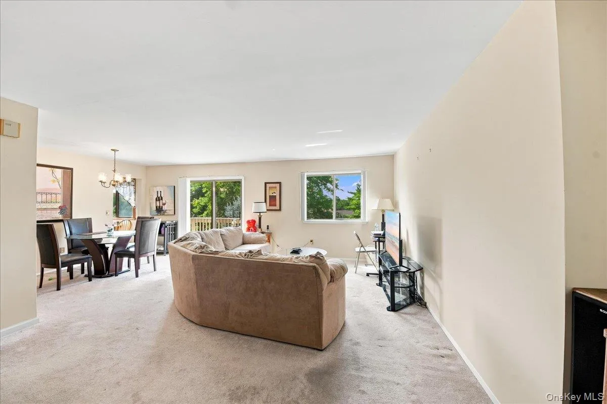 Open-concept living area with neutral carpeting, large windows, and a sliding glass door providing access to an outdoor deck Open-concept living area with neutral carpeting, large windows, and a sliding glass door providing access to an outdoor deck