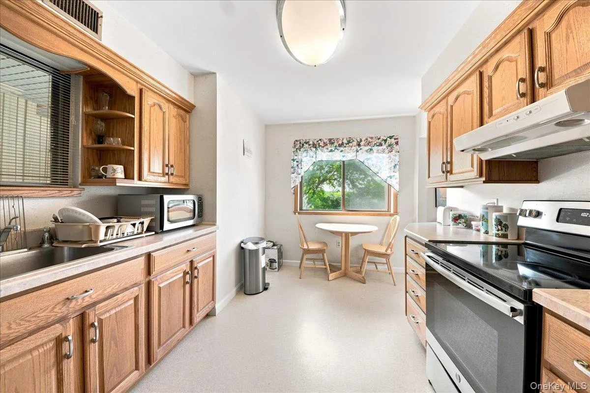 Galley kitchen featuring wood cabinetry, stainless steel appliances including a built-in oven and range, laminate countertops, and a window overlooking the grounds Galley kitchen featuring wood cabinetry, stainless steel appliances including a built-in oven and range, laminate countertops, and a window overlooking the grounds