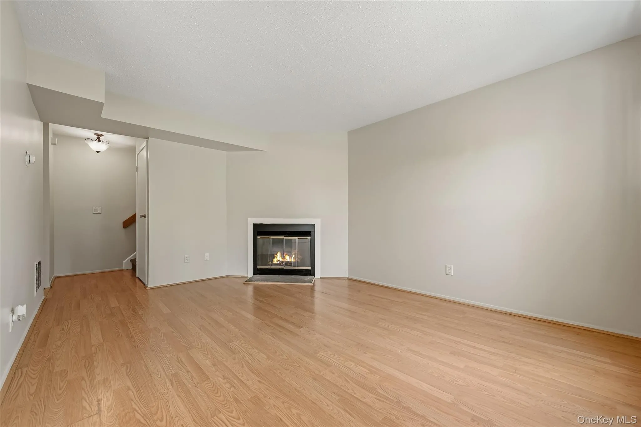 Wood type flooring, corner fireplace with recessed ceiling, neutral wall color, and staircase access Wood type flooring, corner fireplace with recessed ceiling, neutral wall color, and staircase access